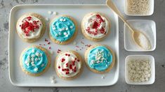 cookies decorated with blue, white and red icing on a tray next to bowls of sprinkles