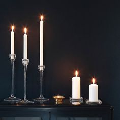 three candles are lit on a black table with two wine glasses and one candle holder