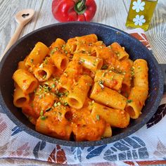 a skillet filled with pasta and sauce on top of a table next to tomatoes