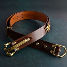 two brown leather belts with brass buckles on a black surface, one is empty and the other has gold hardware