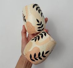 a hand holding two cups with designs on them