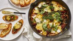 a pan filled with food next to two plates of toast and bread on a table