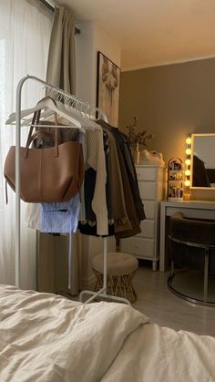 there is a bag hanging on a clothes rack in the bedroom, next to a bed