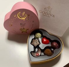 a heart shaped box filled with assorted chocolates on top of a white table