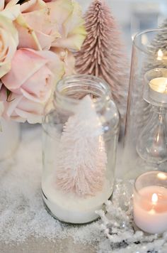 a table topped with candles and vases filled with snow covered christmas trees next to pink flowers