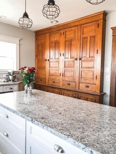 a large kitchen with marble counter tops and wooden cabinets in the back wall, along with hanging lights