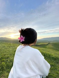 a woman sitting on top of a lush green field next to a grass covered hillside