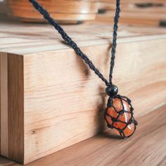 an orange and black bead hangs from a string on a wooden surface with other items in the background