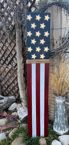 an american flag made out of wood sitting in the grass next to a metal vase