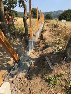 there is a fence that has been built in the dirt near trees and rocks on the ground