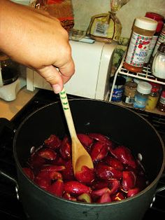 a person stirring plums in a pot on the stove