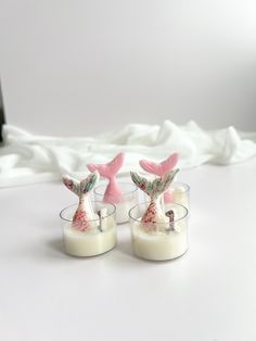 two candles with pink mermaid tails on them sitting next to each other in glass cups