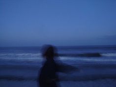 a blurry photo of a person walking on the beach at night with an ocean in the background