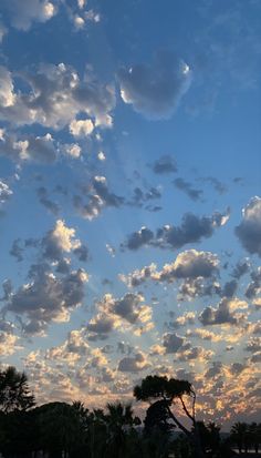 the sky is filled with clouds as the sun sets in the distance behind it and palm trees