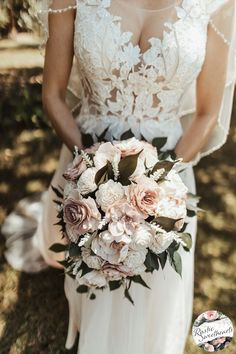 a woman in a wedding dress holding a bouquet of pink flowers and greenery on her arm