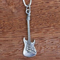 a silver guitar necklace on a wooden table with a chain hanging from it's neck