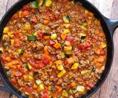 a skillet filled with meat and vegetables on top of a wooden table next to a red frame