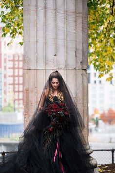 a woman in a black wedding dress with flowers on her head standing next to an old pillar