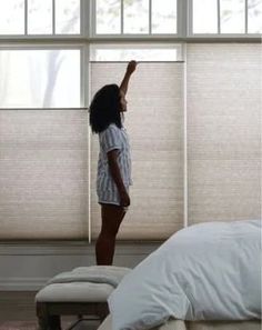 a woman standing in front of a window with her hand up to the ceiling and looking out