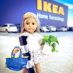 a doll is holding a blue purse and a potted plant in front of a ikea store