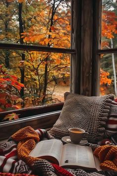 an open book and cup of coffee sit on a blanket in front of a window