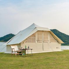 a tent is set up on the grass next to a body of water