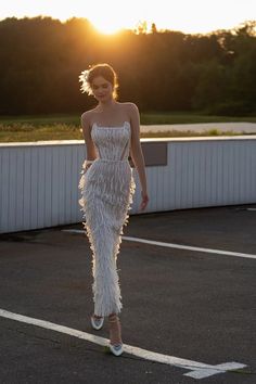 a woman is walking down the runway in a white dress with feathers on her skirt