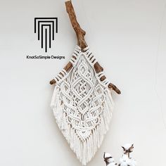 a white macrame hanging on a wall next to some cotton balls and twigs