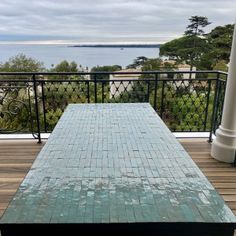 an outdoor table on a deck overlooking the ocean and trees in the distance with no one sitting at it