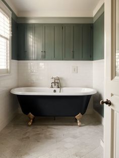 an old fashioned bathtub in a bathroom with green cabinets and white tile flooring