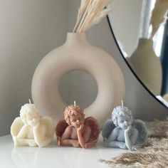 three candles with angel figurines sitting next to each other in front of a mirror