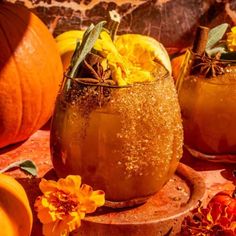 two glasses filled with liquid sitting on top of a wooden table next to pumpkins