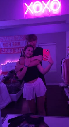 two people are hugging in front of a neon sign that says oxox on it