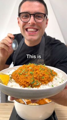 a man holding a bowl with rice and curry on it while smiling at the camera