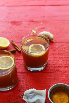 two glasses filled with liquid sitting on top of a red table next to cinnamons