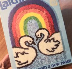 someone is holding up a book with two swans in front of a rainbow on it