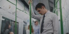 a man standing on a subway train with his hands in his pockets and looking down