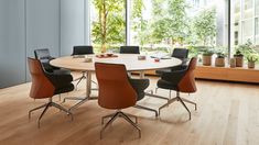 a round table with chairs around it in front of large windows and potted trees