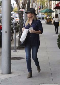 a woman is walking down the sidewalk with a coffee in her hand and wearing a hat