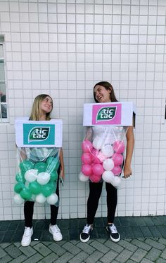 two girls are standing in front of a white wall holding boxes with balloons on them