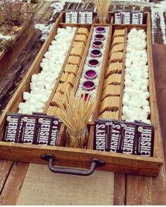 an open wooden box filled with marshmallows and other items on top of a table