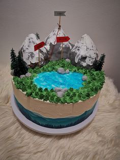 a cake that is shaped like a mountain lake with flags on top and trees in the middle