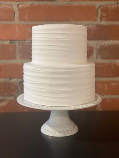 a white frosted cake sitting on top of a table next to a brick wall