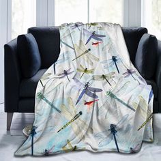 a throw blanket with dragonflies on it sitting in front of a couch next to a window