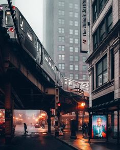 a train traveling over a bridge in the middle of a city at night with people walking on the sidewalk