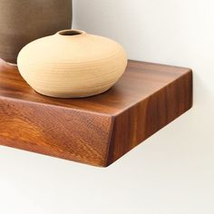 two vases sitting on top of a wooden shelf next to each other in front of a white wall