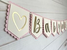 a pink and gold baby shower banner hanging on the wall