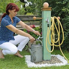 a woman is filling up a bucket with water from a faucet in the garden