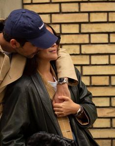 a man and woman standing next to each other in front of a brick wall hugging