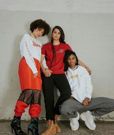 three young women posing for the camera in front of a white wall